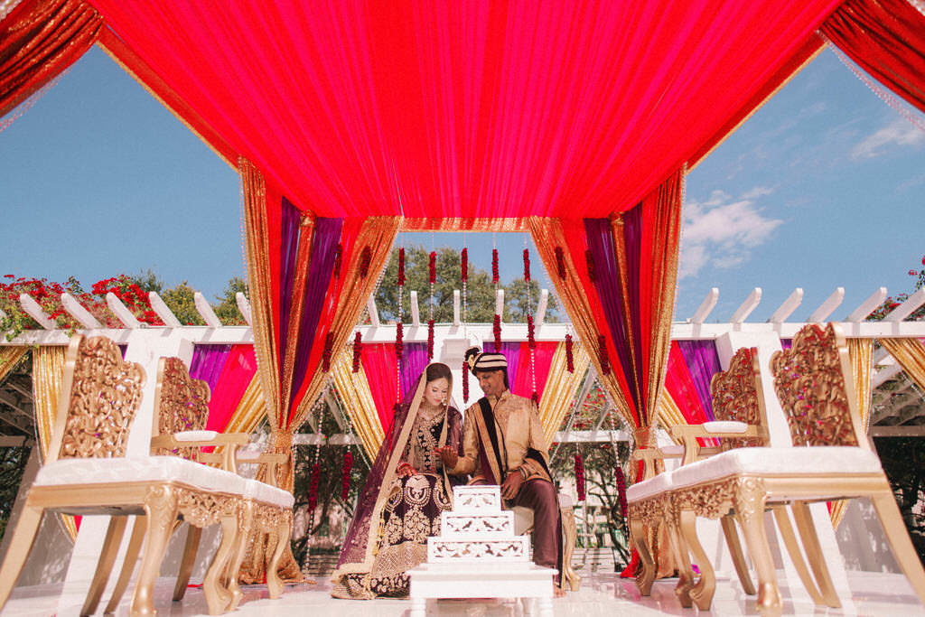 Tampa Bay Luxurious Indian Hindu Traditional Wedding Ceremony Portrait of Bride and Groom Under Elegant Lush Red, Gold and Purple Draping, Elegant Gold and Ivory Cushion Chairs | St. Petersburg Wedding Venue North Straub Park