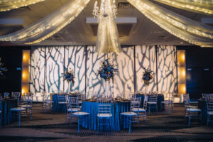 Unique Modern and Contemporary Dark and Dramatic Wedding Reception Decor, String Lighting and White Linen Drapery, Unique Artsy GOBO Projection, Round Tables with Blue Linens, Clear Ghost Acrylic Chiavari Chairs, Tall Glass Vases with Unique Blue and Orange Floral Arrangement Centerpieces | Tampa Bay Boutique Hotel Alba | Wedding Planner Special Moments Event Planning | Wedding Rentals and Chair Decor Gabro Event Services | Styled Shoot