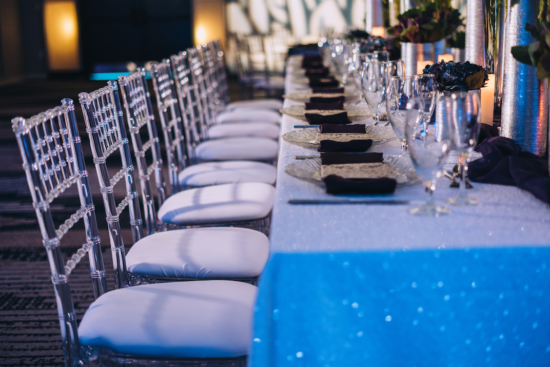 Modern Contemporary Wedding Reception Decor, Long Feasting Table with Blue Sparkle Glitter Linen, Clear Acrylic Ghost Chiavari Chairs | Tampa Bay Wedding Planner Special Moments Event Planning | Wedding Rentals and Chair Decor Gabro Event Services