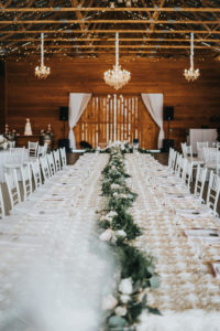 Rustic Chic Barn Wedding Reception Decor, Long Feasting Table with Greenery Garland Table Runner with Ivory Roses, White Chiavari Chairs, Crystal Chandeliers | Tampa Wedding Venue Rafter J Ranch | Tampa Bay Wedding Planner Kelly Kennedy Weddings and Events