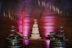 Elegant Five Tier White, Blush Pink Ombre Frosting Roses, Dark Pink Sparkle Top Tier and Embellishment Wedding Cake on Rustic Wooden Barrel Dessert Table with Pink Uplighting | Tampa Wedding Planner Kelly Kennedy Weddings and Events