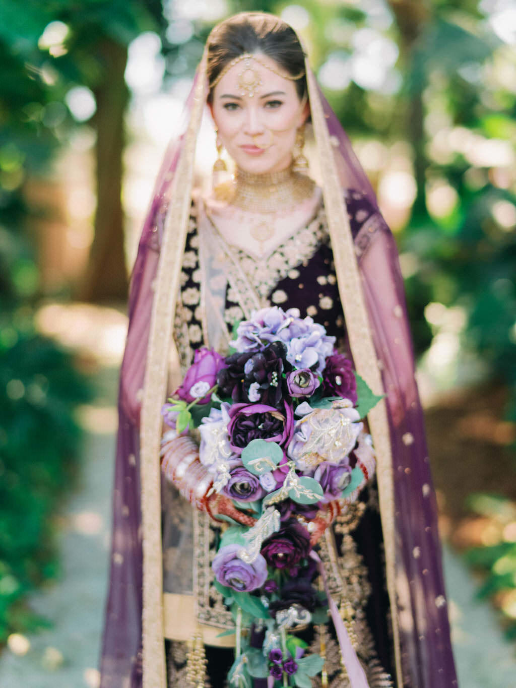 Tampa Traditional Hindu, Indian Colorful Bride, Beauty Wedding Portrait, Extravagant Gold Bridal Jewelry, Custom Purple Velvet and Gold Lehenga and Purple and Gold Bridal Indian Veil Holding Dark Purple, Plum, Lilac and Green Leaf with Gold Accent Floral Bouquet