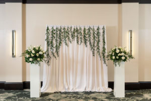 Classic Rustic Elegant Tampa Ballroom Wedding Ceremony Decor, White Drapery Backdrop Hanging Greenery, White Pedestals with Greenery and Ivory and White Roses Floral Arrangements | South Tampa Wedding Venue The Epicurean Hotel