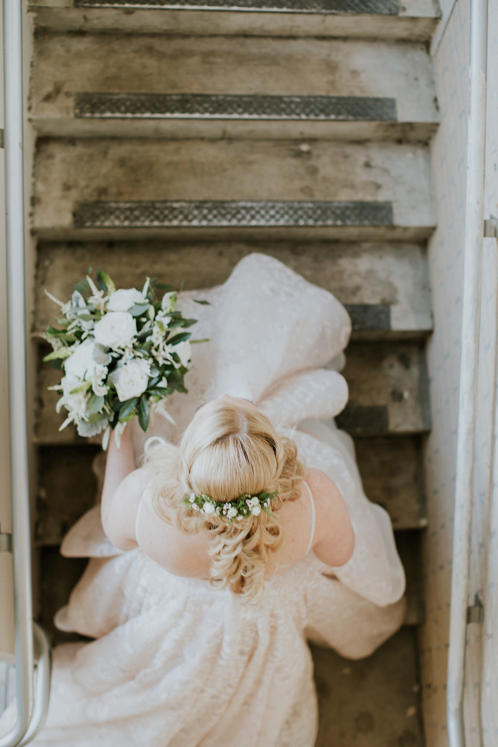 Creative Florida Bride Going Up the Stairs From Above Wedding Portrait Holding Organic Greenery and Ivory Floral Bridal Bouquet, Greenery Floral Hairpiece and Half Updo