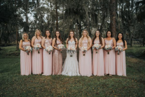 Tampa Bay Bride in Lace and Illusion V Neckline Wedding Dress, Bridesmaids in Blush Pink Sparkle Glitter Sequin Bodice Dresses Holding White and Pink Roses with Dusty Miller Leaves | Parrish Wedding Venue Rafter J Ranch