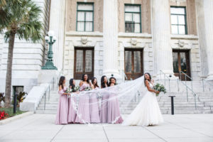 Creative Outdoor Bride and Bridal Party Wedding Portrait, Bridesmaids in Matching Off the Shoulder Pink Dresses Holding Bride's Veil | Steps of Tampa Hotel Wedding Venue Le Meridien | Wedding Photographer Lifelong Photography Studio