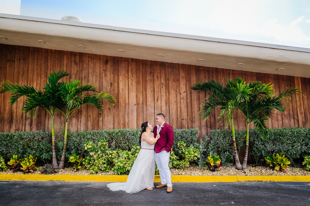 Tampa Bride in Flowy Lace and Tulle Strapless Wedding Dress with Satin Belt and Groom in Burgundy Red Suite Jacket and White Dress Pants First Look Wedding Portrait | St. Petersburg Wedding Venue Postcard Inn on the Beach