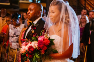 Modern Florida Bride and Father Walk down the Ceremony Aisle, Holding Romantic Floral Bouquet Blush Pink Roses, Burgundy Flowers, Plum Hibiscuses, Quartz and Magenta Blooms, Dark Greenery and Gold Accents | Historic Downtown St. Pete Industrial Wedding Venue NOVA 535