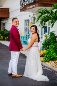 Tampa Bride in Flowy Lace and Tulle Strapless Wedding Dress with Satin Belt and Groom in Burgundy Red Suite Jacket and White Dress Pants First Look Wedding Portrait | St. Petersburg Wedding Venue Postcard Inn on the Beach