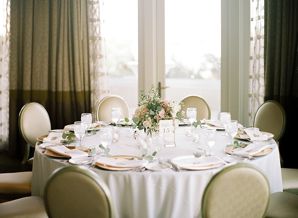 Classic Formal Ballroom Wedding Reception Decor, Round Tables with White Linens, Gold Chargers, Blush Pink and White Roses, Eucalyptus and Greenery Low Floral Centerpiece with Gold Table Number Sign | Downtown St. Pete Wedding Venue The Birchwood