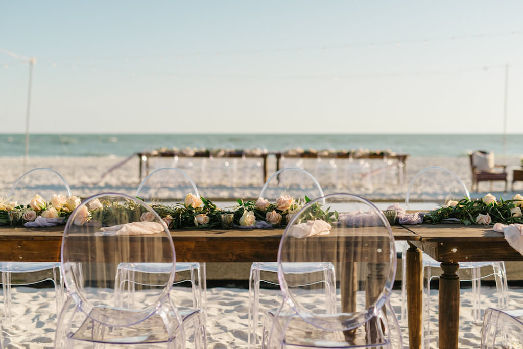 Outdoor Beachfront Wedding Reception with Long Wooden Feasting Table and Ghost Chairs with Garland of Roses and Greenery | Resort at Longboat Key Club Sarasota Area Wedding Venue