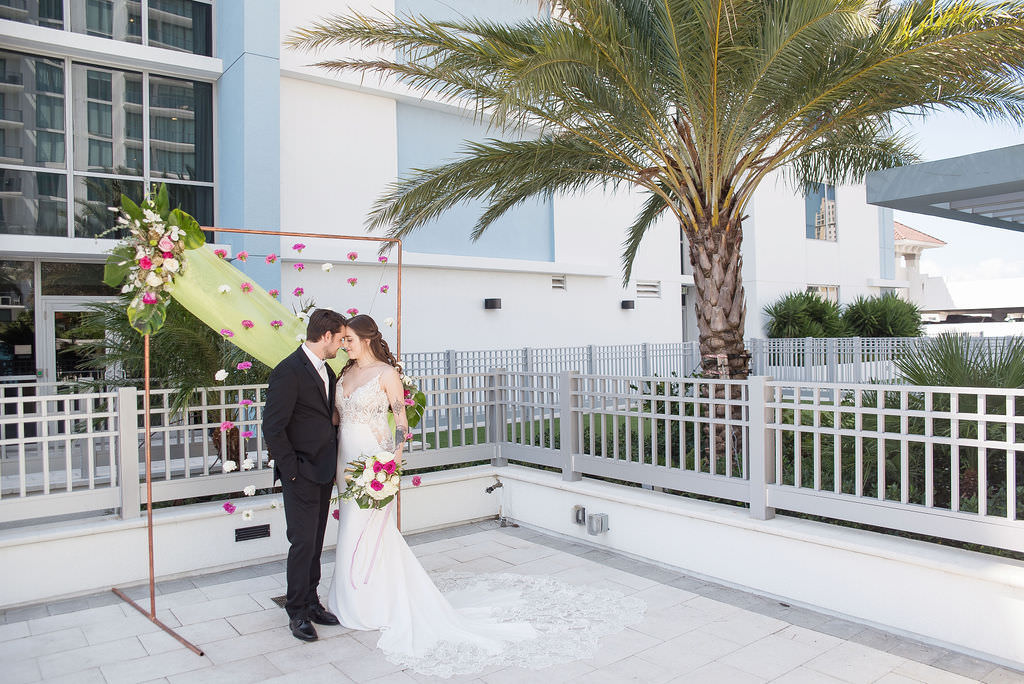 Modern Florida Bride and Groom Wedding Portrait, Colorful Tropical Wedding Ceremony Decor, Copper Arch, Fuschia Pink and White Hanging Carnations, Lime Green Draping, Pink and Ivory Roses, Monstera Palm Leaf Floral Arrangement | Tampa Bay Wedding Photographer Kristen Marie Photography | Hotel Wedding Venue Hyatt Place Downtown St. Pete | Wedding Florist Brides N Blooms | Wedding Attire Nikki's Glitz and Glam Boutique | Outside the Box Event Rentals | Wedding Hair and Makeup LDM Beauty Group