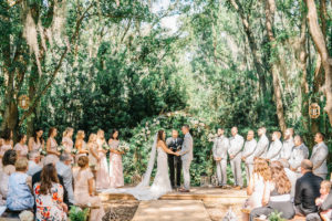 Enchanting Outdoor Wedding Ceremony Under Canopy of Oak Trees, Bridal Party at Alter, Bride and Groom Exchanging Wedding Vows Portrait | Whimsical Tampa Bay Venue Florida Rustic Barn Weddings