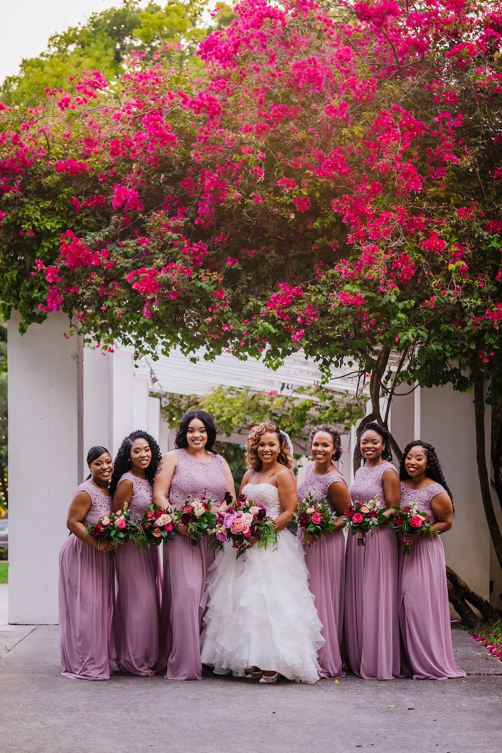 Tampa Bay Bride and Bridesmaids in Modern David's Bridal Long Purple Dresses, Bride Wearing Strapless Ballgown Wedding Dress, Holding Romantic Textured Floral Bouquet, With Blush Pink Roses, Burgundy Flowers, Hibiscuses, Quartz and Magenta Florals, Dark Greenery and Gold Accents, at Downtown St. Pete Straub Park