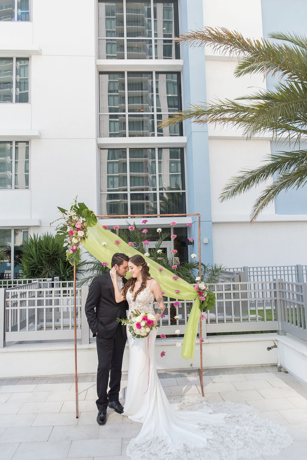 Modern Bride and Groom Wedding Portrait, Colorful Tropical Wedding Ceremony Decor, Copper Arch, Fuschia Pink and White Hanging Carnations, Lime Green Draping, Pink and Ivory Roses, Monstera Palm Leaf Floral Arrangement | Tampa Bay Wedding Photographer Kristen Marie Photography | Hotel Wedding Venue Hyatt Place Downtown St. Pete | Wedding Florist Brides N Blooms | Wedding Attire Nikki's Glitz and Glam Boutique | Outside the Box Event Rentals | Wedding Hair and Makeup LDM Beauty Group