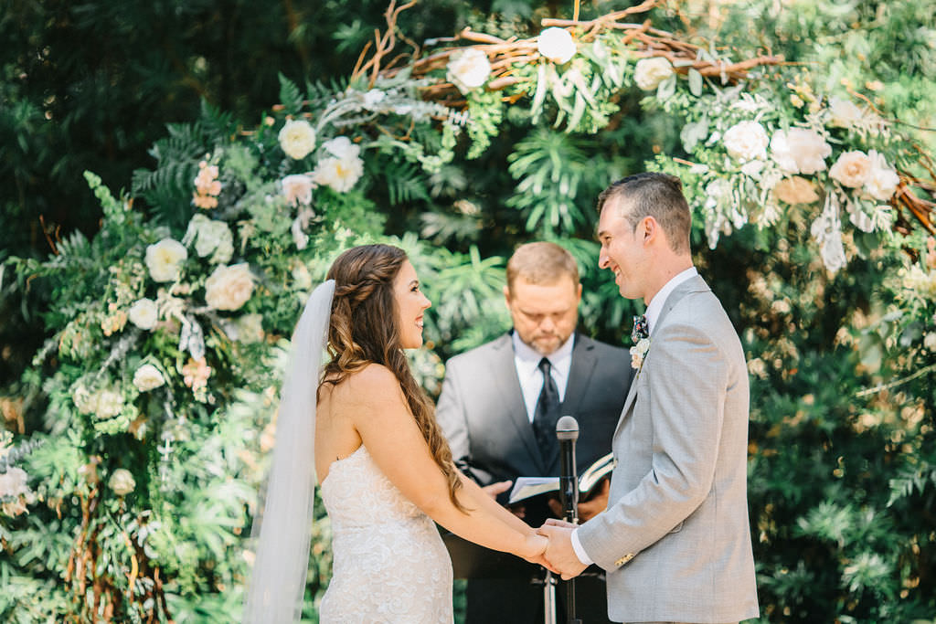 Tampa Bay Bride and Groom Exchange Wedding Vows Outdoors in Garden Ceremony with Lush Pink and Ivory Flowers, Greenery | Plant City Wedding Venue Florida Rustic Barn Weddings