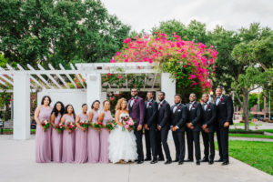Tampa Bay Bride and Groom with Modern Wedding Party in Straub Park in Downtown St. Pete, Bridesmaids in David's Bridal Long Purple Dresses, Holding Romantic Textured Floral Bouquet, With Blush Pink Roses, Burgundy Flowers, Hibiscuses, Quartz and Magenta Florals, Dark Greenery, Groom Styled in Plum Suit Jacket and Bowtie, American Basketball Player Davante Gardner