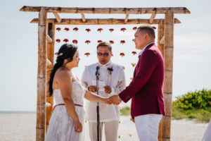 Tropical Tampa Bride and Groom Exchanging Wedding Vows During Ceremony Portrait, Bamboo Arch with Hanging Red and Pink Carnation Flowers