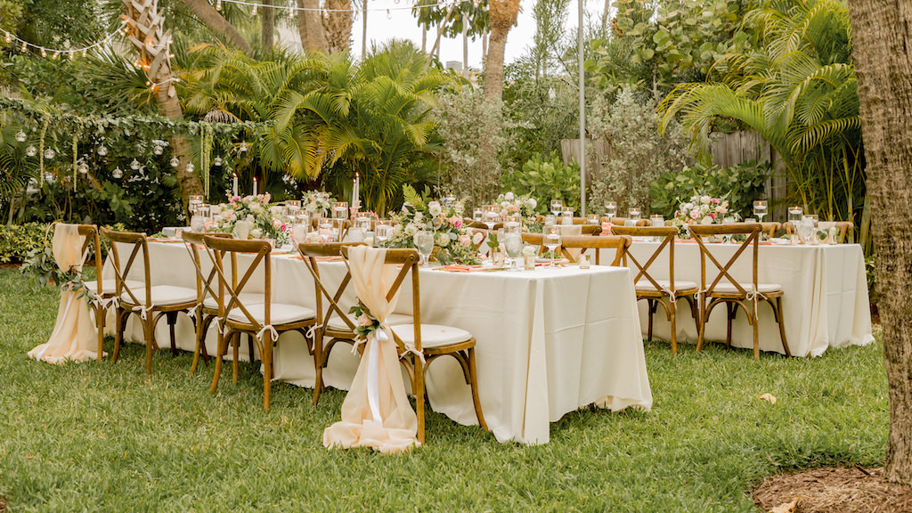 Tampa Garden Inspired Outdoor Wedding Reception Decor, Long Feating Tables, Ivory Linens, Wooden Cross Back Chair with Blush Pink Sashes and Greenery Ties