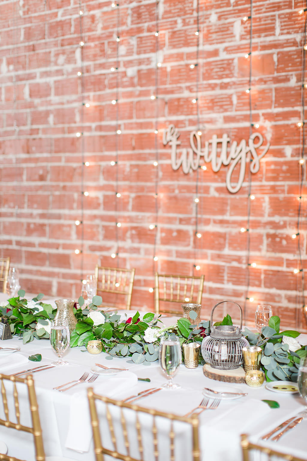 Rustic Chic Inspired Wedding Decor at Feasting Table, Romantic Greenery Eucalyptus Leaves Garland Centerpiece, Nature Inspired Lanterns, Gold Chiavari Chairs, Against Exposed Red Brick Wall with Indoor String Lighting | Florida Historic Wedding Venue NOVA 535 | St. Petersburg Wedding Photographers Shauna and Jordon Photography