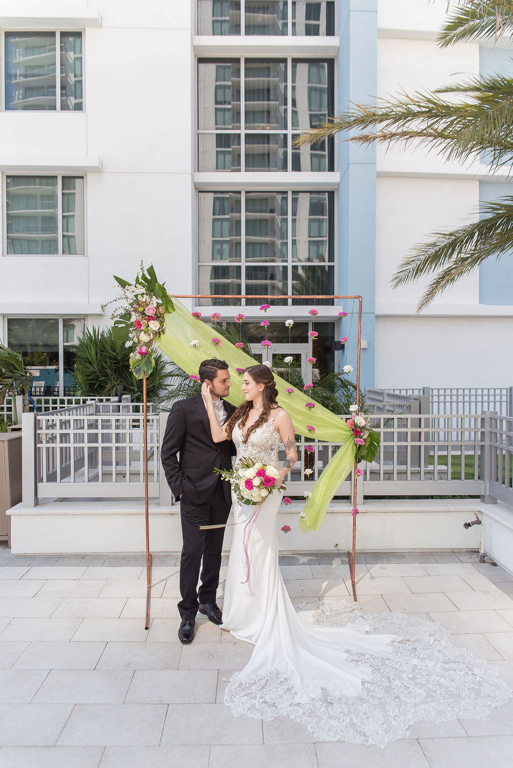 Modern Bride and Groom Wedding Portrait, Colorful Tropical Wedding Ceremony Decor, Copper Arch, Fuchsia Pink and White Hanging Carnations, Lime Green Draping, Pink and Ivory Roses, Monstera Palm Leaf Floral Arrangement | Tampa Bay Wedding Photographer Kristen Marie Photography | Hotel Wedding Venue Hyatt Place Downtown St. Pete | Wedding Florist Brides N Blooms | Wedding Attire Nikki's Glitz and Glam Boutique | Outside the Box Event Rentals | Wedding Hair and Makeup LDM Beauty Group