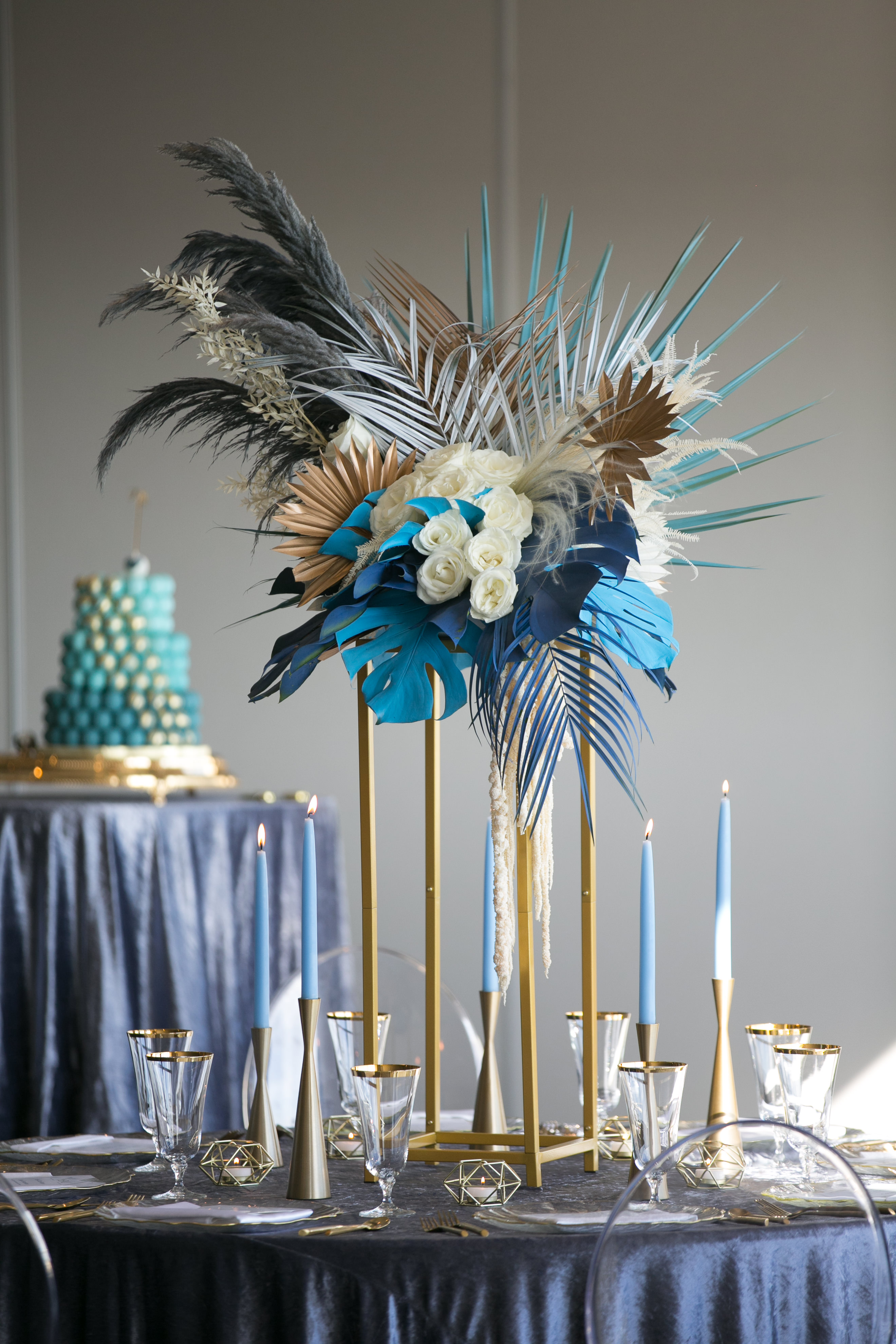 Whimsical Unique Tropical Wedding Reception Decor, Round Tables with Midnight Blue Linen, Tall Gold Candlesticks with Blue Candles, Tall Gold Geometric Stands with White Roses, Blue Monstera and Palm Tree Leaves and Feathers and Ghost Chair Seating | Tampa Wedding Chair Rentals Gabro Event Services | Velvet Navy Blue Table Linens Kate Ryan Event Rentals | Wedding Photographer Carrie Wildes Photography | Wedding Planner and Florist John Campbell Weddings | Tampa Wedding Venue Centre Club