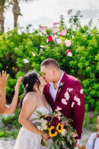 Fun St. Pete Bride and Groom Kissing Wedding Portrait, Pink Flower Petals, Bride Holding Organic Tropical Yellow Sunflowers, Purple, Red and Pink Floral Bouquet