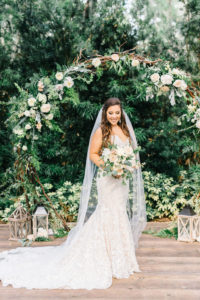 Romantic Tampa Bay Bride Beauty Wedding Portrait, Soft and Whimsical Organic Garden Bridal Bouquet with Ivory Roses, Blush Pink Flowers, Sage Green Leaves, Lace Wedding Dress, Standing In Front of Circular Wedding Arch with Lush Greenery | Florida Rustic Barn Weddings