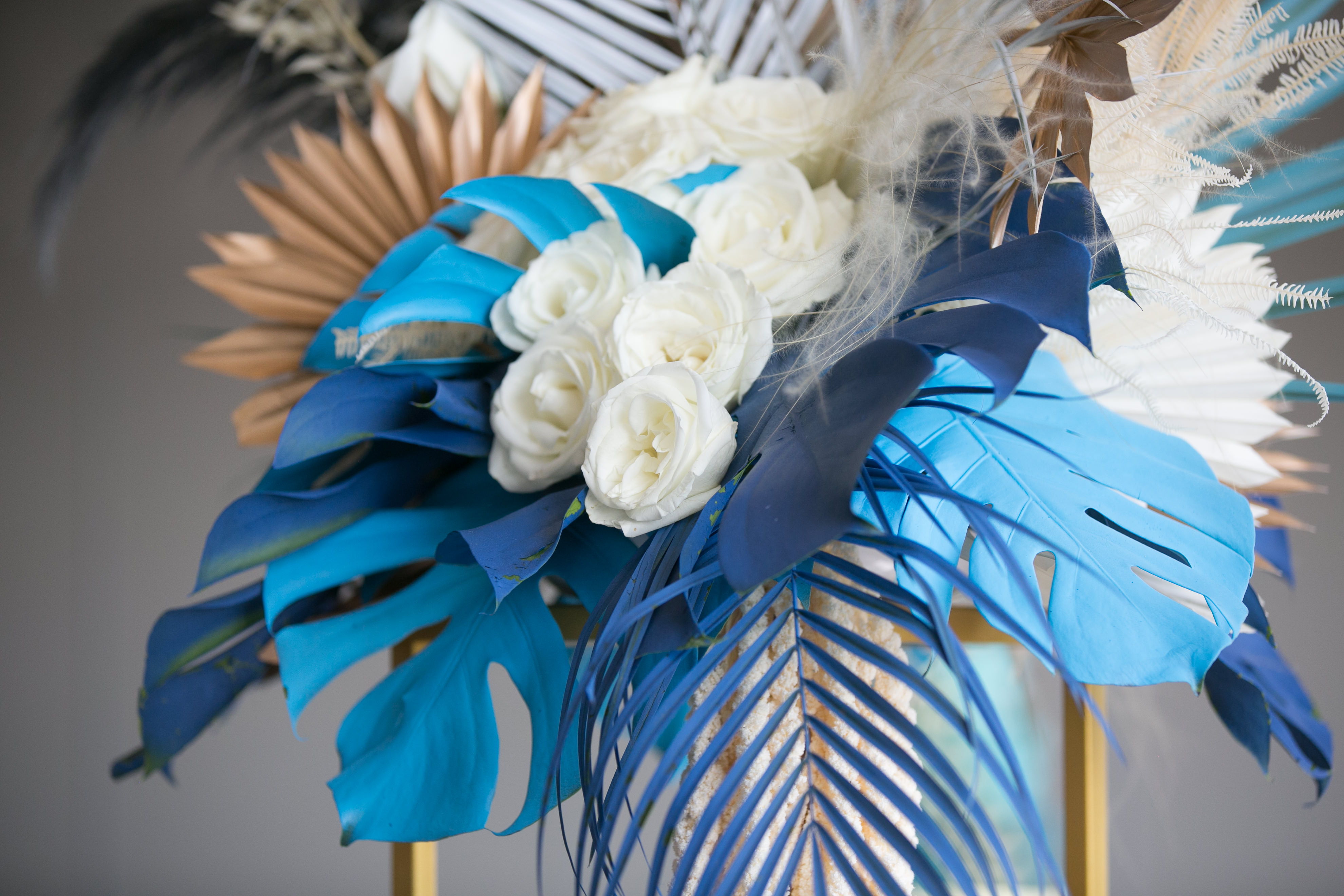 Whimsical Unique Wedding Reception Decor, Dusty Blue Monstera, Navy Blue Palm Tree Leaves, White Roses, Feathers and Gold Accents Floral Centerpiece | Tampa Wedding Planner and Florist John Campbell Weddings | Wedding Photographer Carrie Wildes Photography