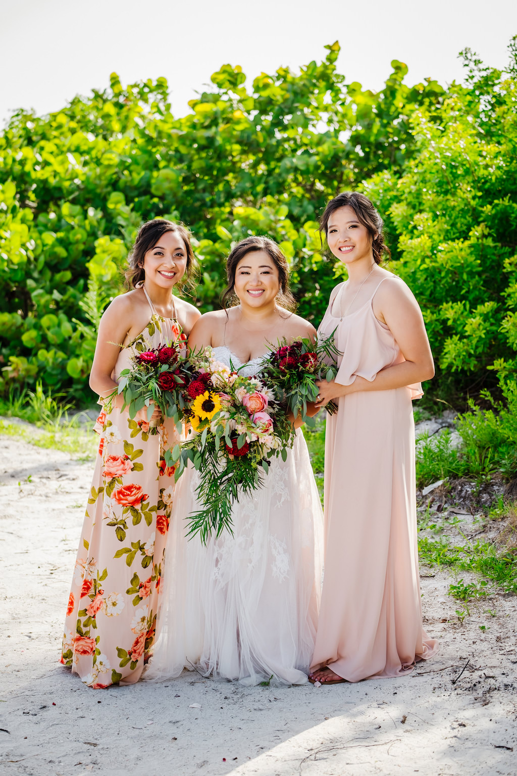 St. Pete Bride Holding Tropical Organic Yellow Sunflowers, Pink and Red Roses with Greenery Floral Bouquet, Bridesmaids in Mix and Match Blush Pink and Floral Print Floor Length Dresses Beachfront Wedding Portrait