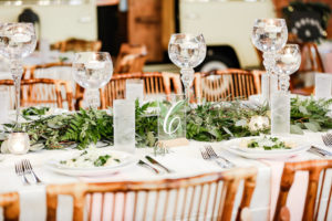 Industrial Boho Chic Wedding Reception Decor, White Linens, Bamboo Wooden Chairs, Greenery Garland Table Runner, Tall Glass Candlesticks, Clear Acrylic Table Number Sign | Tampa Bay Wedding Photographer Lifelong Photography Studio | Wedding Planner Special Moments Event Planning | Wedding Tables, Chairs, Linen Rentals Gabro Event Services