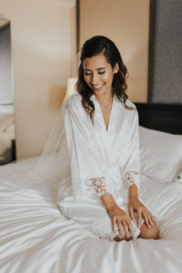Bride Beauty Wedding Portrait on Hotel Bed Wearing Silk White and Lace Robe and Veil