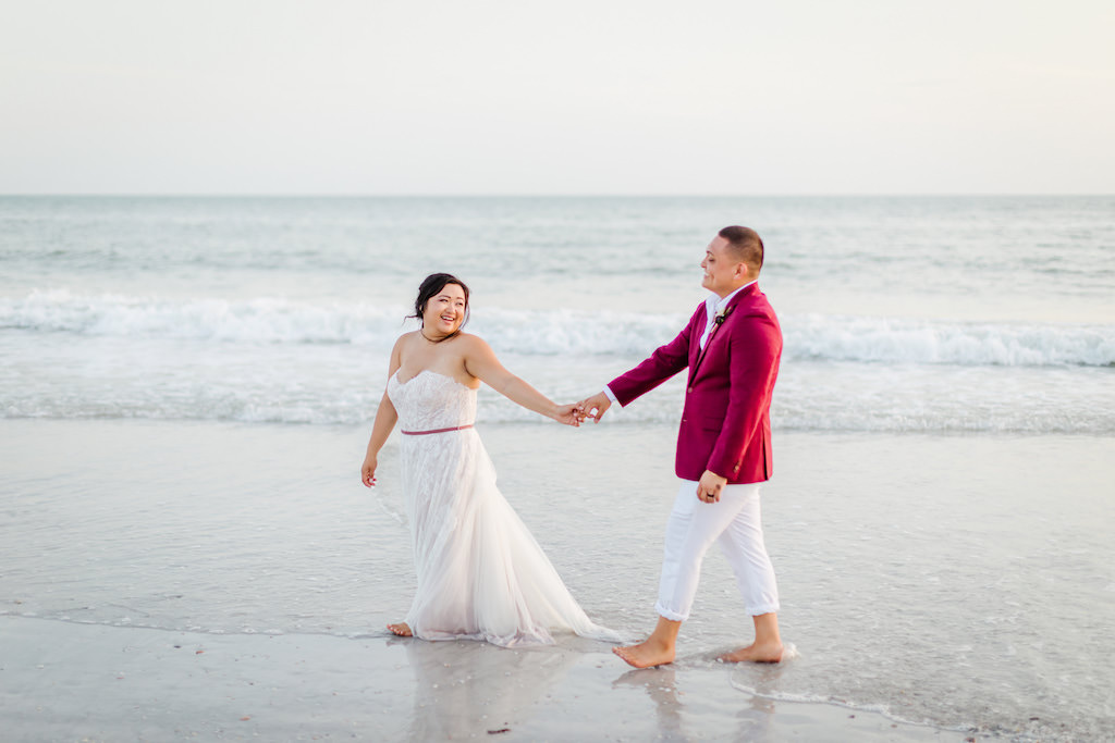 Waterfront Bride in Flowy Strapless Lace and Tulle Wedding and Dress, Groom in Red Suit Jacket and White Dress Pants St. Pete Beach Wedding Portrait