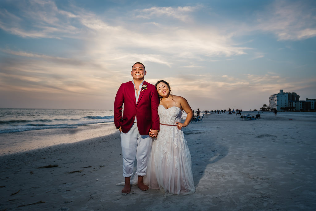 Waterfront Bride in Flowy Strapless Lace and Tulle Wedding and Dress, Groom in Red Suit Jacket and White Dress Pants St. Pete Beach Sunset Wedding Portrait