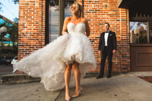 INSTAGRAM Fun Bride and Groom Outdoor St. Pete Wedding Portrait, Bride in Ruffle High Low Wedding Skirt and Strapless Dress, Clear Pointed Toe Wedding Shoes, Groom in Black Tuxedo | Wedding Dress Shop Isabel O'Neil Bridal Collection