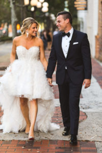 Modern Bride and Groom Holding Hands Wedding Portrait, Bride in Ruffle High Low Skirt Strapless Sweetheart Wedding Dress, Groom in Black Tuxedo | Ines DiSanto Wedding Dress Isabel O'Neil Bridal Collection