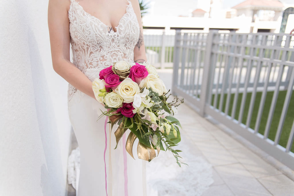 Bride Holding Fuchsia Pink and Ivory Rose with Greenery, Palm Leaf, and Metallic Gold Painted Monstera Leaf Floral Bridal Bouquet in Low V Neckline Lace and Illusion Fitted Wedding Dress |Tampa Bay Wedding Photographer Kristen Marie Photography | St. Pete Wedding Florist Brides N Blooms | Palm Harbor Wedding Attire Nikki's Glitz and Glam Boutique