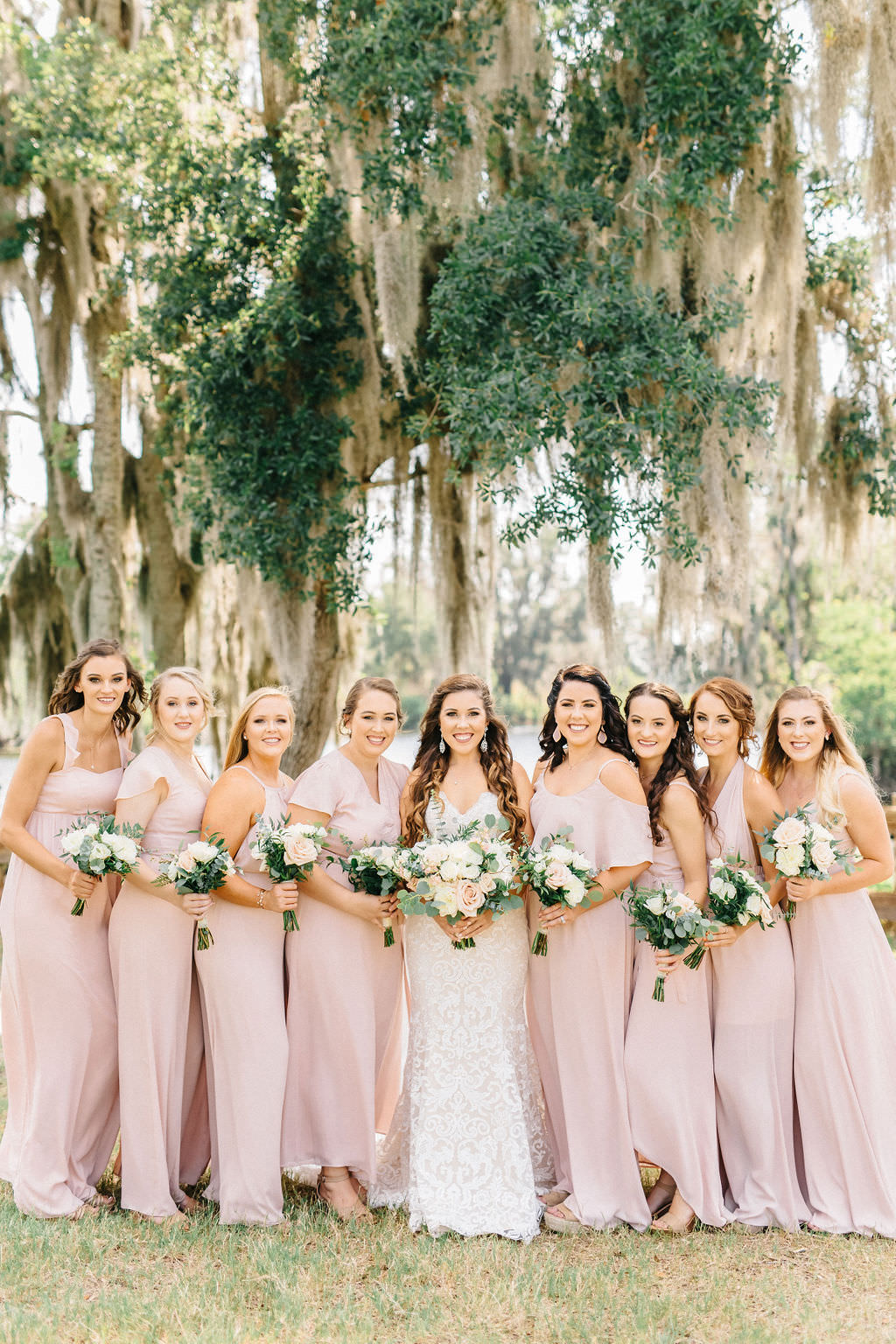 Tampa Bay Bride and Bridesmaids Under Mossy Oak Tree, Bridesmaids in Mix and Match Blush Pink Show Me Your MuMu Long Dresses, Holding Whimsical Ivory and Pink Floral Bouquets with Greenery | Plant City Outdoor Wedding Venue Florida Rustic Barn Weddings