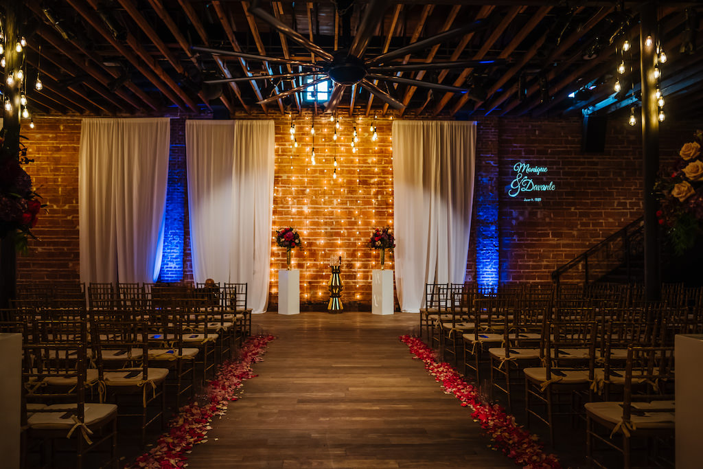 Romantic Garden Indoor Wedding Decor, Exposed Red Brick Wall Ceremony Backdrop with Vintage Hanging Lights, White Draping, Gold Chiavari Chairs, Blush Pink, Burgundy, Plum, Quartz and Magenta Florals, Flower Petals Lining Aisle | Historic Downtown St. Pete Industrial Wedding Venue NOVA 535