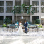 Unique Tropical Wedding Ceremony Decor, Acrylic Ghost Chair Seating, Bride and Groom Standing in Front of Fountain with Palm Tree Leave Arrangements | Tampa Wedding Chair Rentals Gabro Event Services | Wedding Planner and Florist John Campbell Weddings | Wedding Photographer Carrie Wildes Photography | Tampa Wedding Venue Centre Club