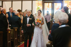 Florida Bride and Father Walking Down Traditional Church Wedding Ceremony Aisle Holding Whimsical Orange, Pink Roses and Greenery Floral Bouquet | Tampa Bay Wedding Hair and Makeup Femme Akoi Beauty Studio | St. Pete Wedding Florist Bruce Wayne Florals
