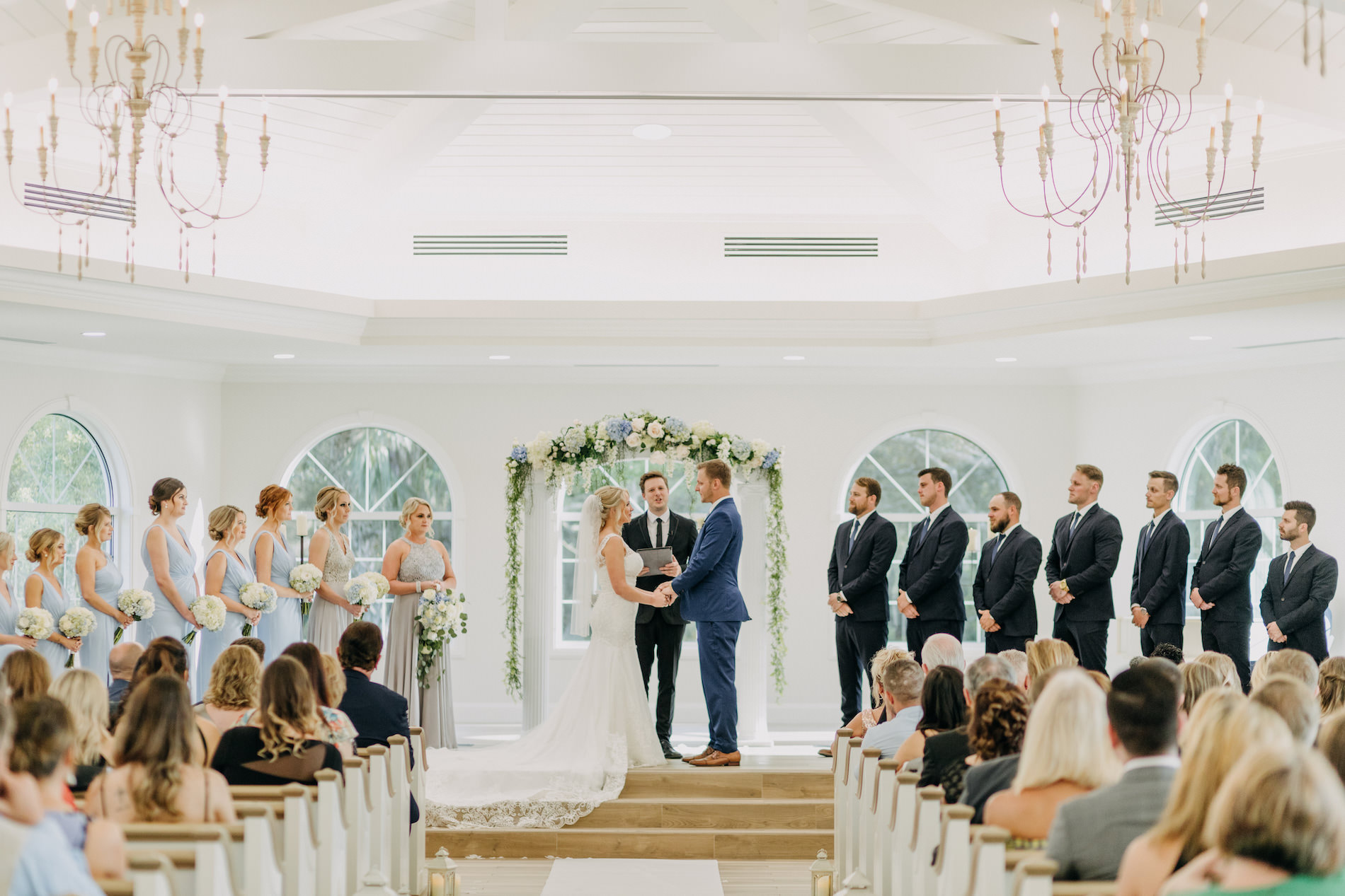 Florida Bride and Groom Exchanging Vows During Traditional Church Wedding Ceremony Portrait Under Greenery and White and Powder Blue Floral Arch | Tampa Wedding Venue Harborside Chapel