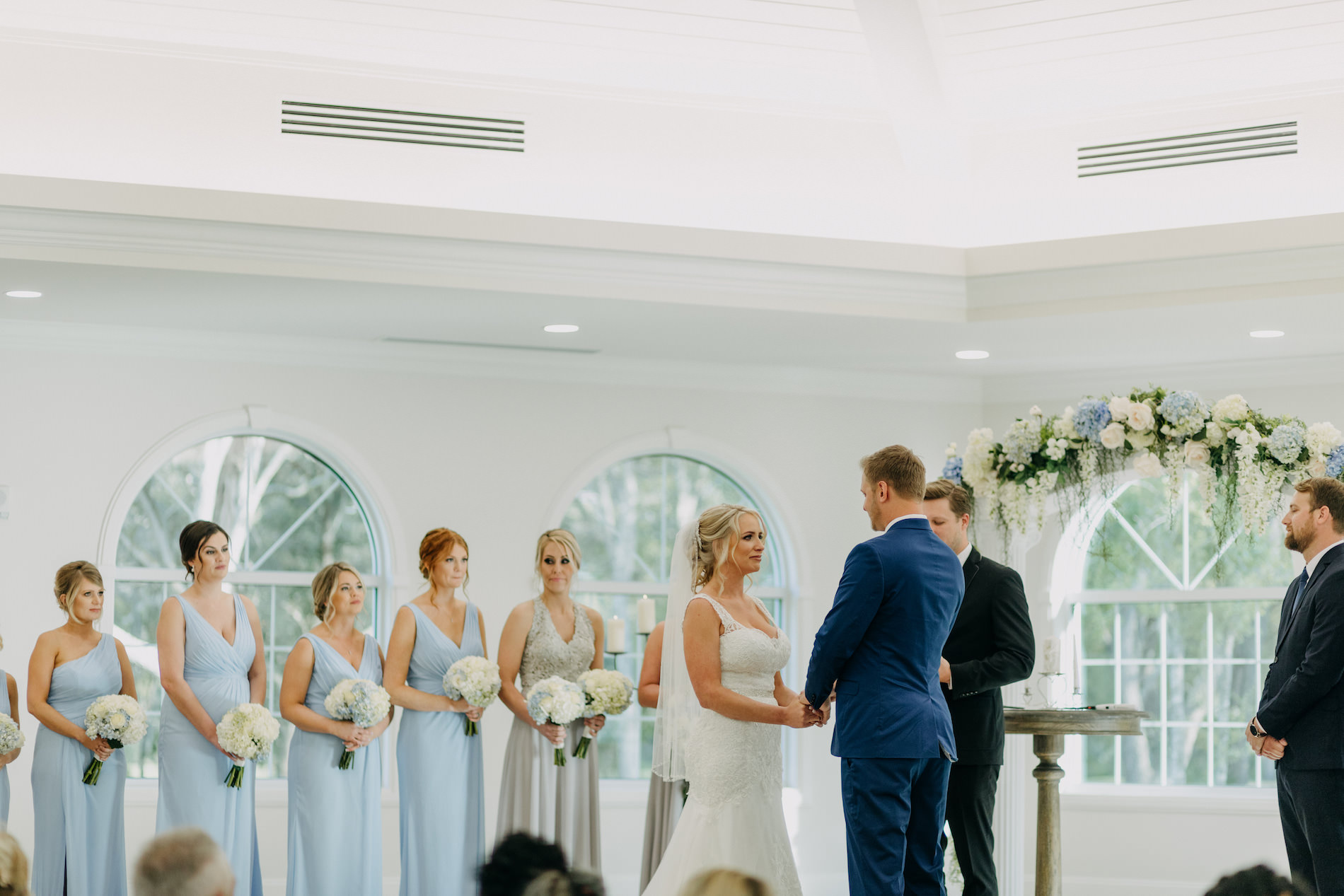 Florida Bride and Groom Exchanging Vows During Traditional Church Wedding Ceremony Portrait Under Greenery and White and Powder Blue Floral Arch | Tampa Wedding Venue Harborside Chapel