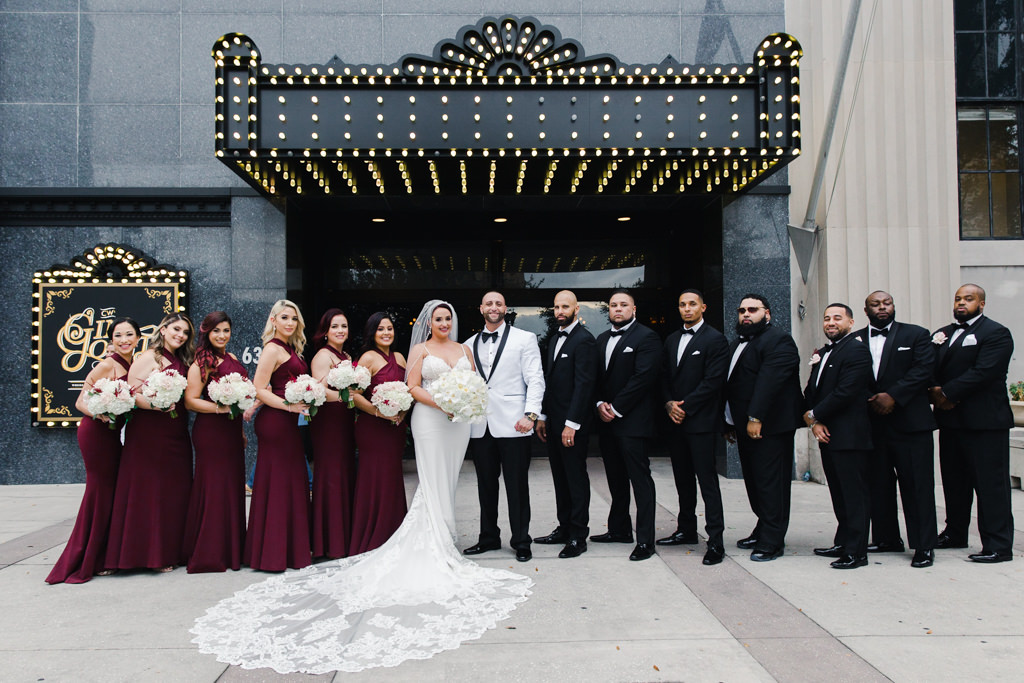 Modern Bride in Lace and Illusion V Neckline with Spaghetti Straps and Long Train Wedding Dress, Groom in White Tuxedo, Bridesmaids in Matching Maroon Dresses, Groomsmen in Black Tuxedos Wedding Party Portrait | Tampa Bay Wedding Florist Gabro Event Services