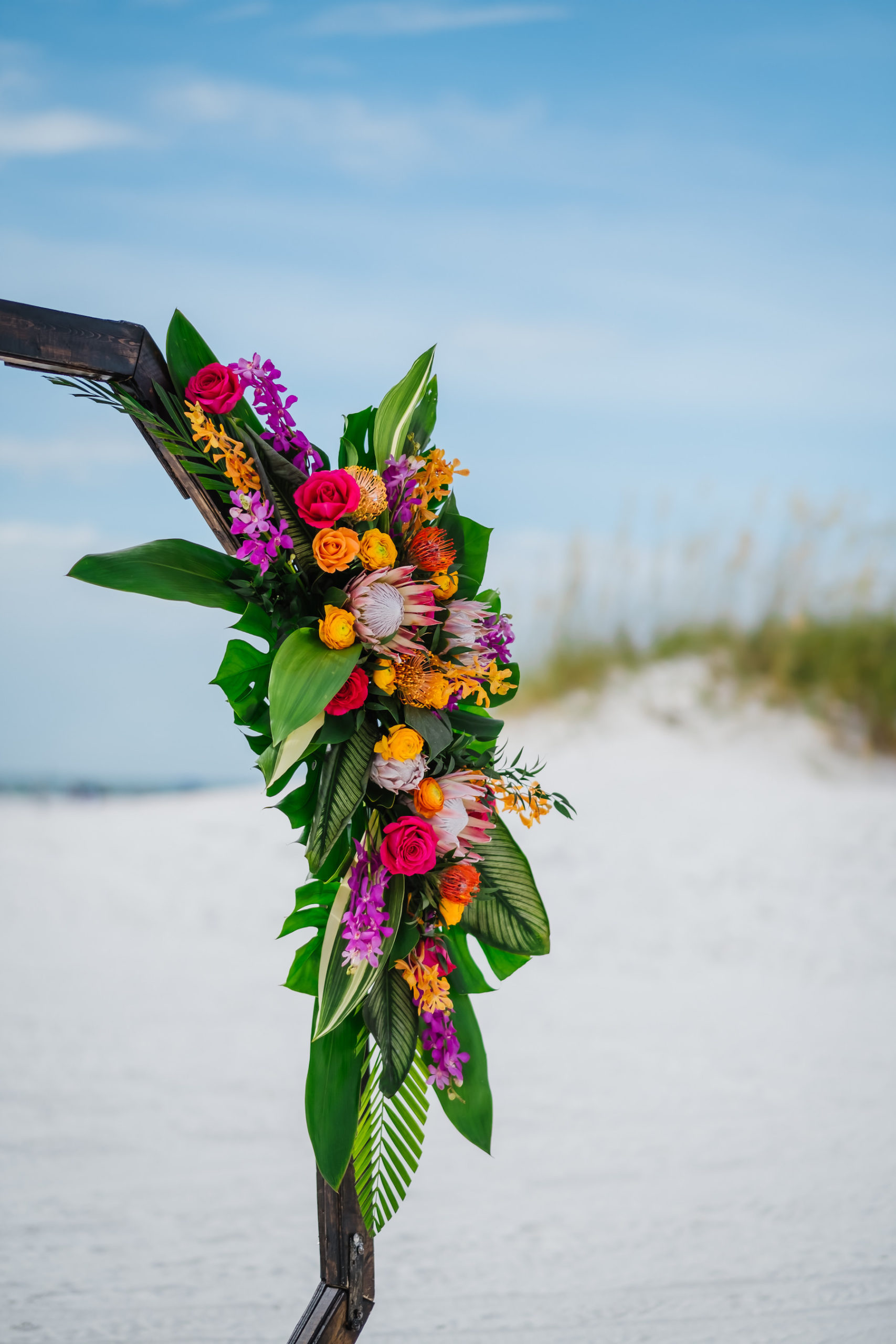 Clearwater Beach Waterfront Beachfront Wedding Reception Decor, Tropical Floral Arrangements, King Proteas, Palm Fronds, Monstera Palm Leaves, Orange, Pink, Purple and Yellow Floral Arrangements on Geometric Octagonal Ceremony Arch | Florida Beach Wedding Ceremony Decor Ideas