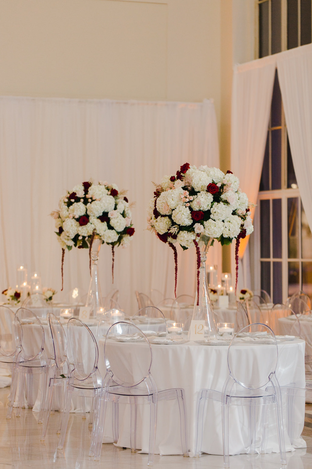 Elegant Wedding Reception Decor, Round Tables with White Tablecloths, Acrylic Ghost Chairs, Tall Glass Vase with White and Blush Pink Hydrangeas with Dark Red Hanging Amaranthus | Tampa Bay Wedding Venue The Vault | Wedding Florist and Rentals Gabro Event Services