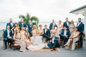 Tampa Bay Waterfront Wedding Party Portrait, Bridesmaids in Mix and Match Blush Pink, Neutral and Champagne Dresses, Groomsmen in Blue Suits with Pink Bowties, Bride in Lace and Illusion Neckline Watters Wedding Dress Holding Whimsical Orange and Pink Roses with Greenery Floral Bouquet | St. Petersburg Wedding Hair and Makeup Femme Akoi Beauty Studio