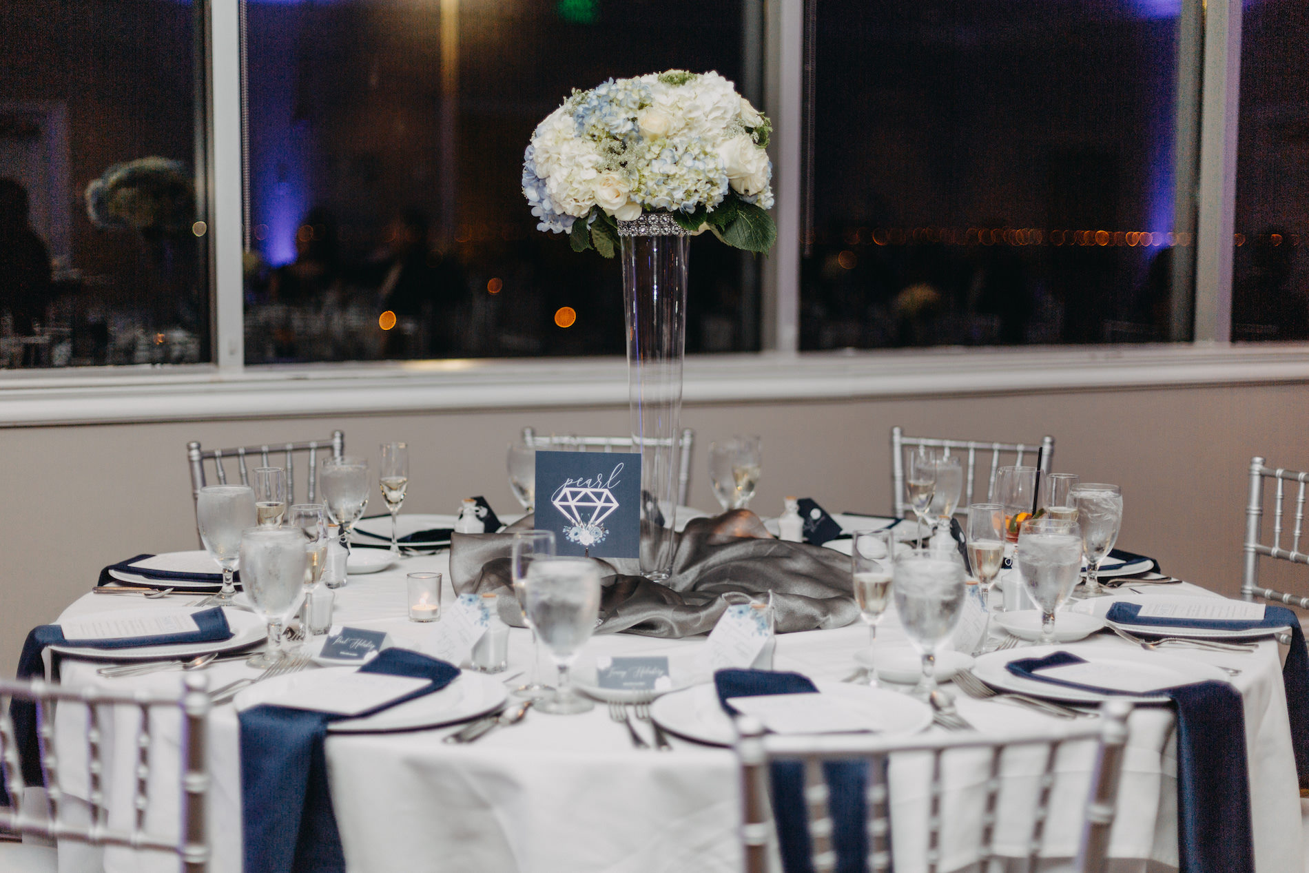 Classic Elegant Wedding Reception Decor, Round Table with White Tablecloth, Navy Blue Linens, Silver Chiavari Chairs, Tall Glass Cylinder Vase with White and Blue Hydrangeas Floral Centerpiece | Tampa Bay Wedding Venue Centre Club