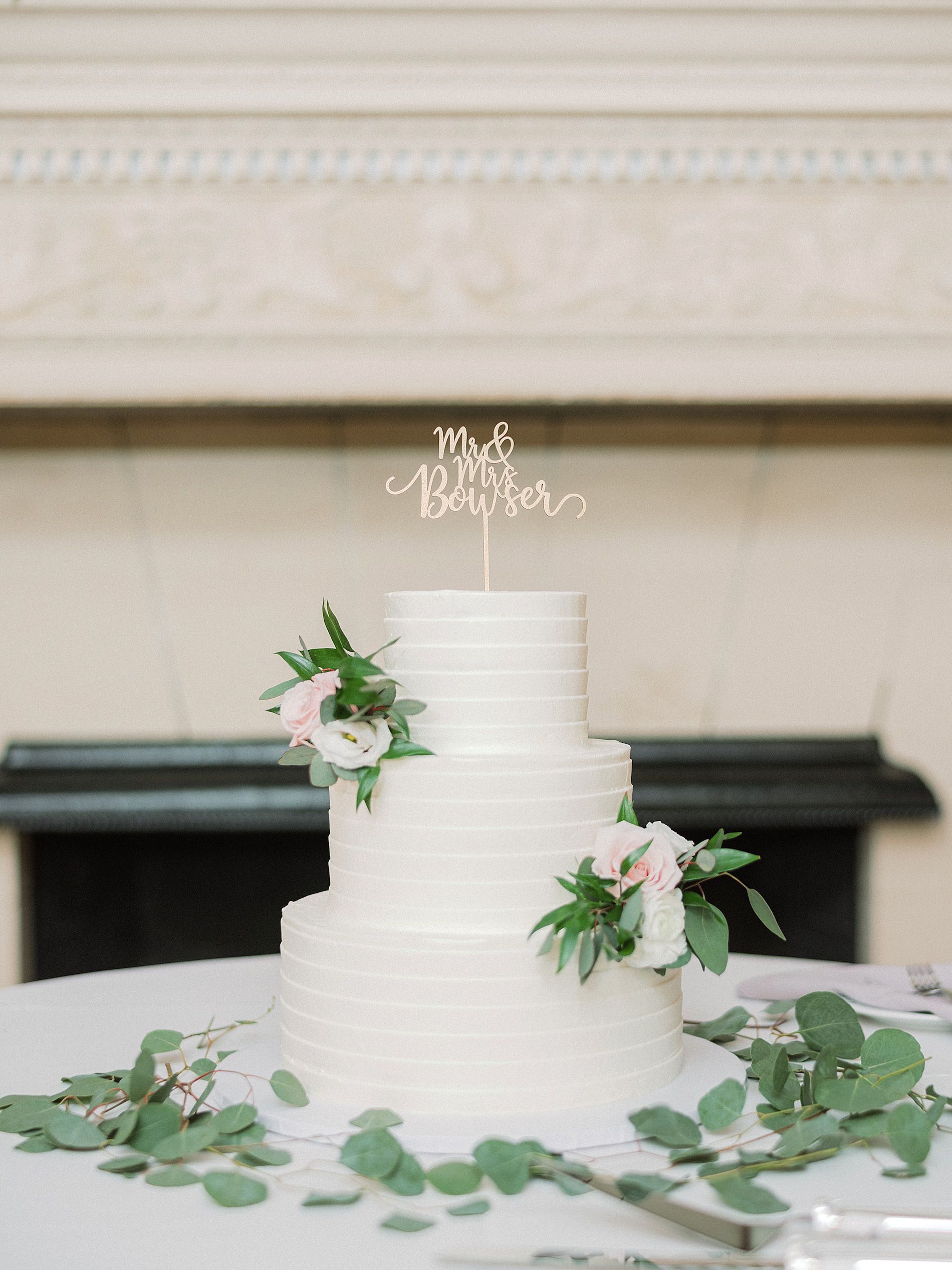 White Three Tier Wedding Cake with White and Blush Pink Roses, Eucalyptus Decor and Custom Laser Cut Cake Topper