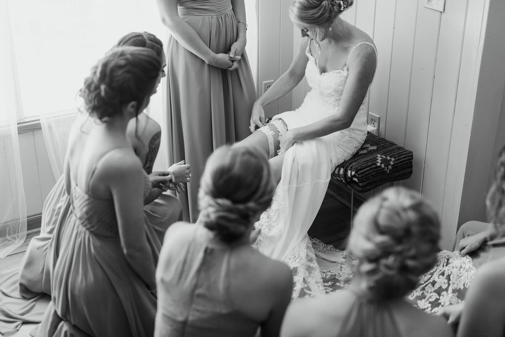 St. Petersburg Bride Putting on Lace Garter Wearing Lace V Neckline with Spaghetti Straps Classic Wedding Dress with Bridesmaids Portrait | Tampa Bay Wedding Photographer Kera Photography | Wedding Dress Shop Truly Forever Bridal